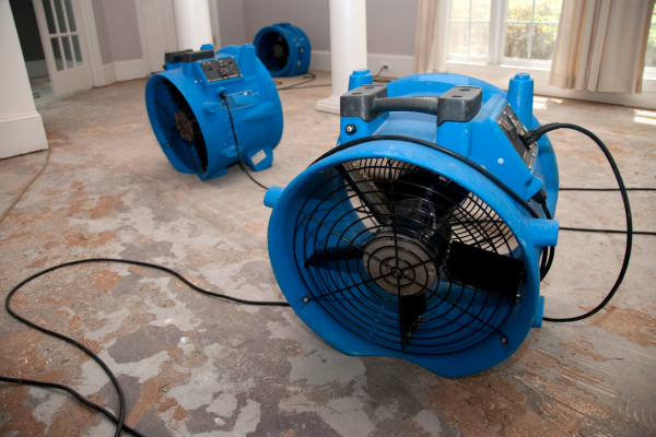 Close-up of industrial air movers and drying equipment placed on a water-damaged floor.